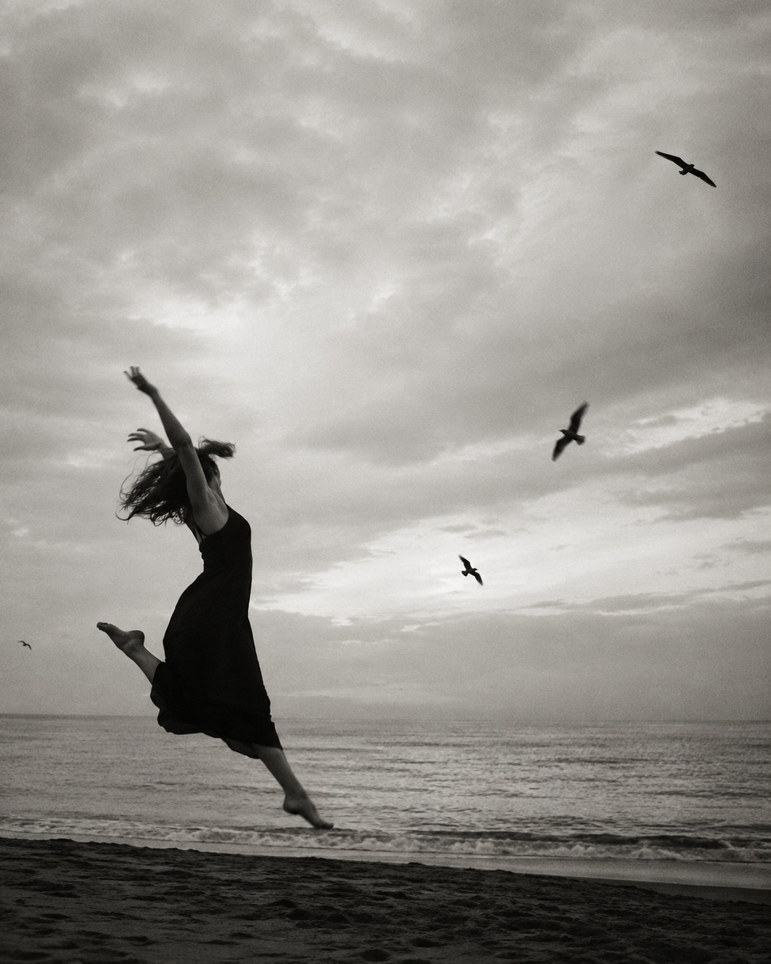 Mujer saltando en la orilla del mar, fotografía en blanco y negro