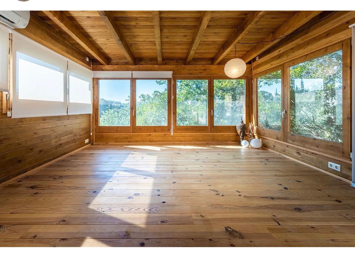 Interior de una casita de madera con grandes ventanales y luz natural